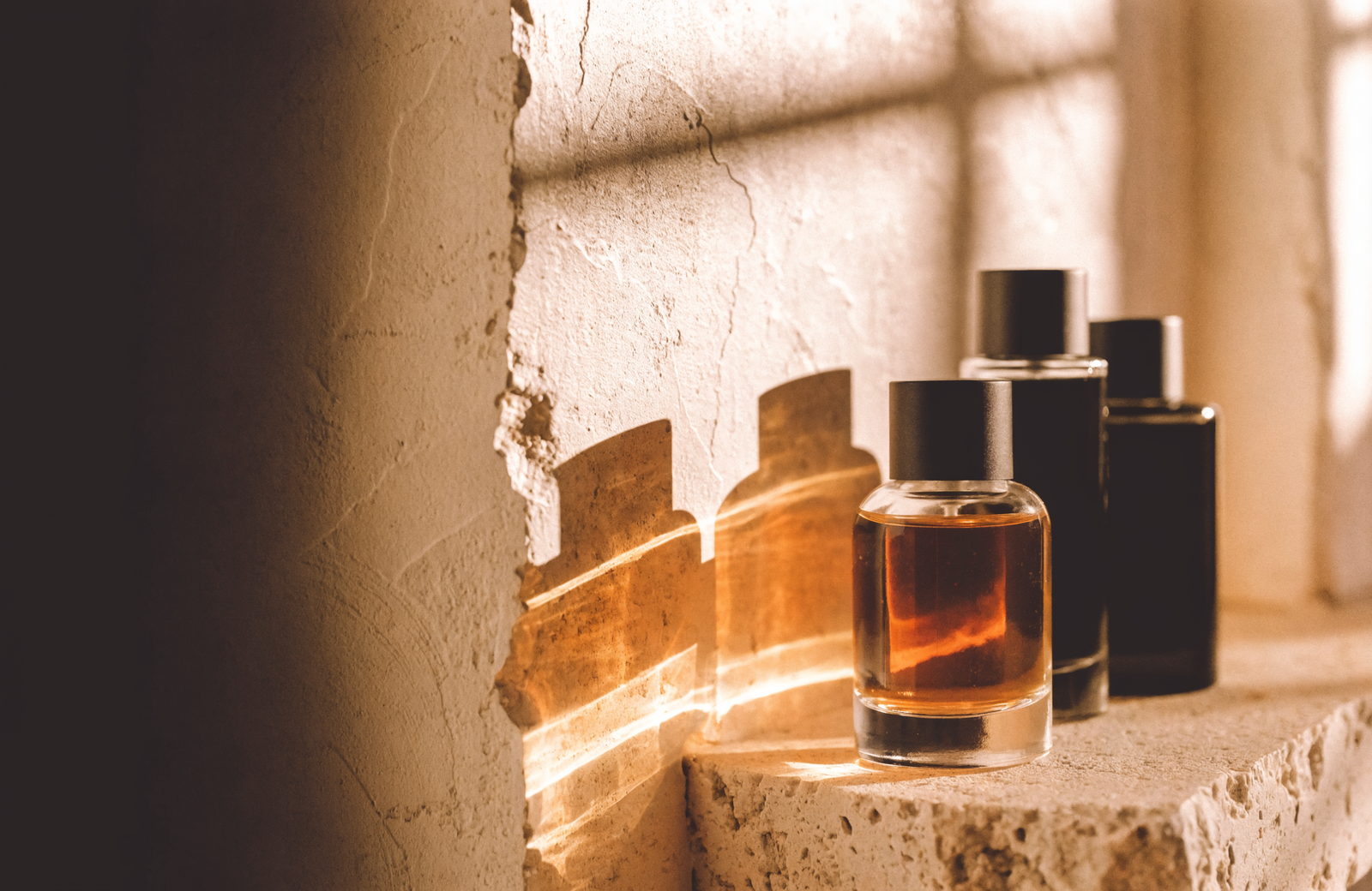 Three glass perfume bottles on a travertine ledge in warm late-afternoon light
